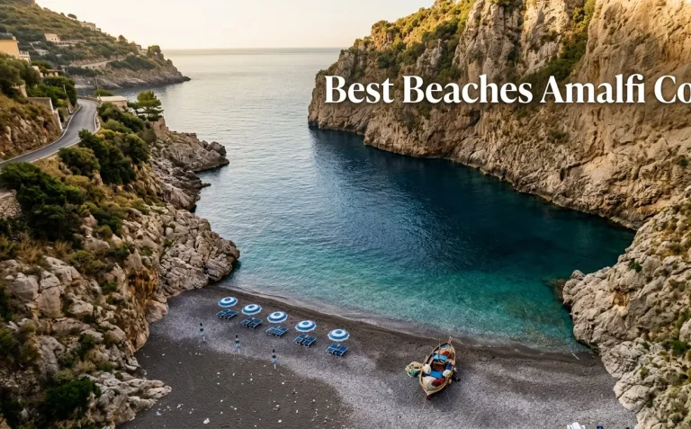 Aerial photo of the dramatic Marina di Praia pebble cove on the Amalfi Coast with blue umbrellas and a fishing boat.